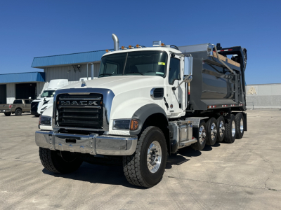 Dump truck front-left angle showing Mack GR64F cab and multiple rear axles with dump bed.