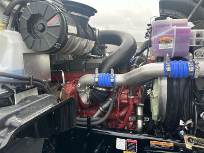 Mack GR64F engine bay showing diesel engine with red block, air intake, blue silicone hoses, coolant reservoir, and auxiliary components.