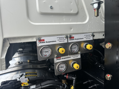 Panel with dual pressure gauges and yellow adjustment knobs mounted on Mack GR64F chassis, showing ‘Liftiable Suspensions’ branding on the label.