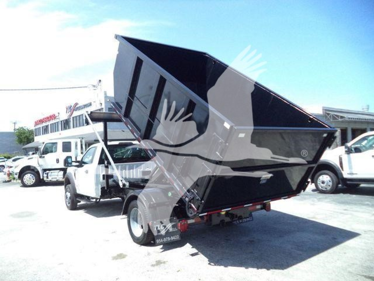 Ford F-550 dump truck in rolled-back position showing dump bed and rear wheels; side view with other trucks in background.