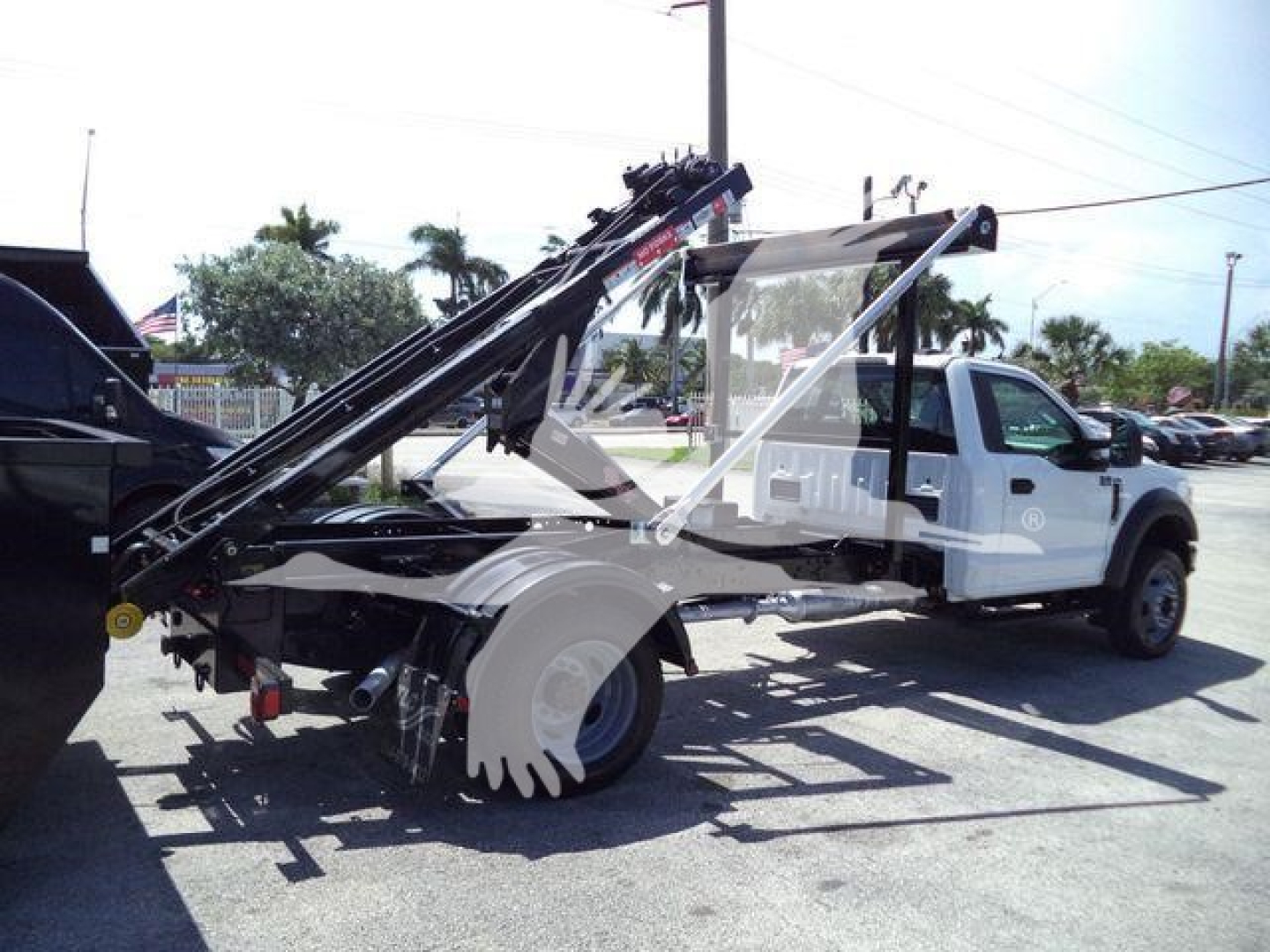 Ford F-550 roll-off truck with hydraulic loading arms viewed from the side, showing the rear hoisting mechanism and twin rear tires.