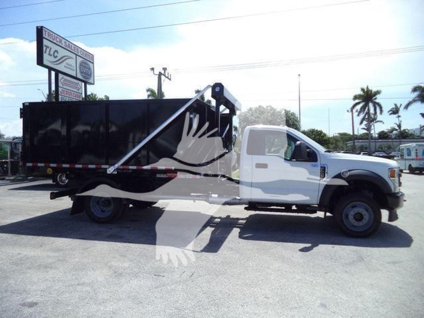 Ford F-550 roll-off truck with a black dump bin, white cab, and deployed lifting mechanism.
