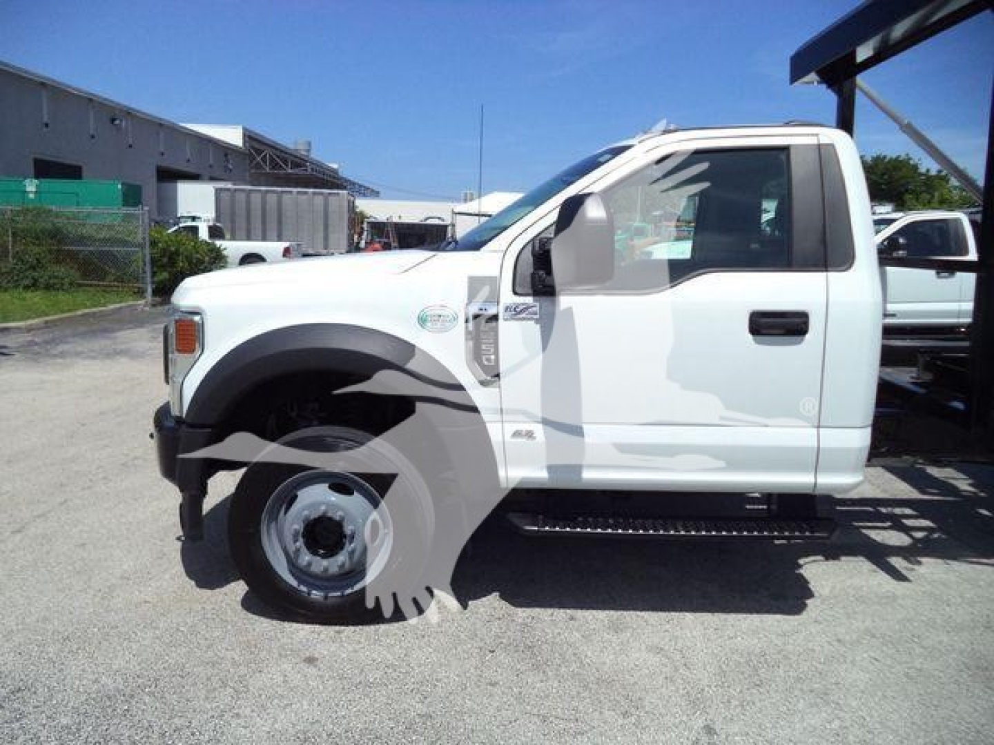 Ford F-550 roll-off truck side view with white cab, front fender badge, black step bar, and dual rear wheels.