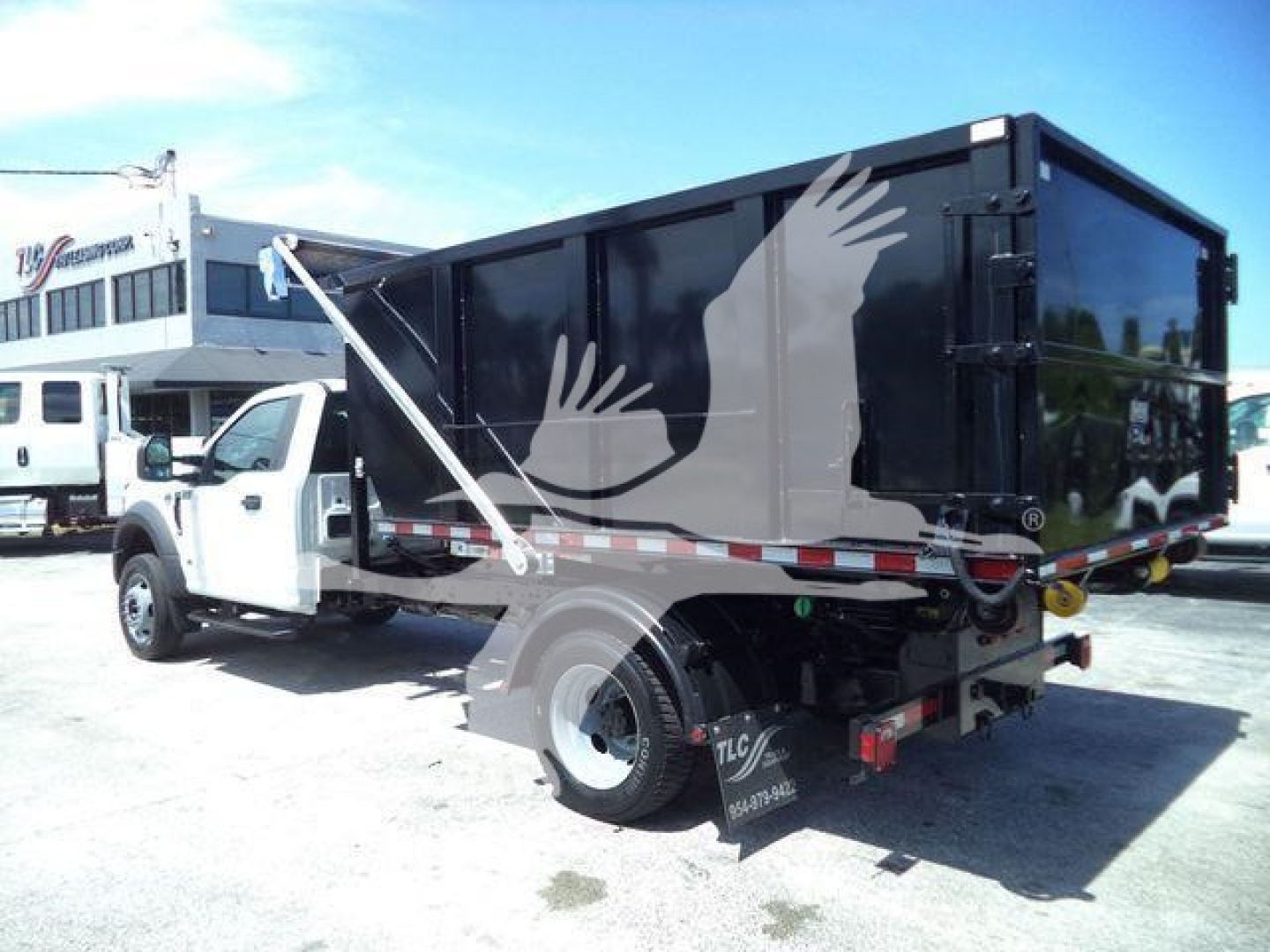 Truck setup showing a black roll-off dump bed on a white Ford F-550 with stock number T04065FM; features include rear bumper, taillights, and hydraulic components.