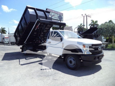 Ford F-550 dump truck in service showing dump bed raised on a roll-off chassis with white cab and black bed.