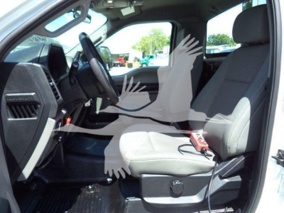 Cab interior of a 2020 Ford F550 rolloff truck showing front seats and dashboard with steering wheel; light gray cloth seats, keys on seat, driver-side door open.