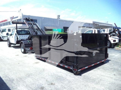 Truck bed of a black roll-off container in a parking lot with other trucks in background