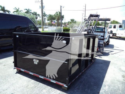 Flatbed roll-off truck bed with black metal sides and white bird graphic, attached to a tow vehicle in a lot.