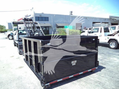 Ford F-550 roll-off truck body in a loading yard showing a black dump box with reflective striping and multiple trucks in background.