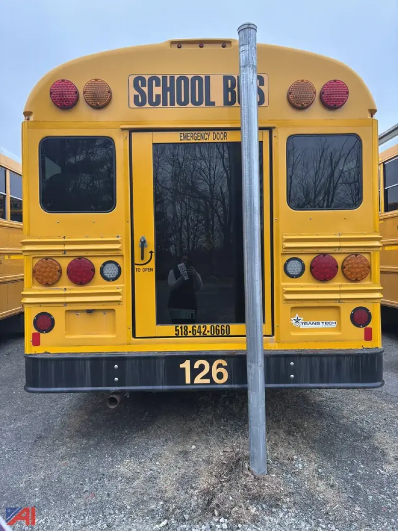 School bus rear view with yellow body, 'SCHOOL BUS' sign, emergency exit window, rear lights, bumper, and a vertical pole in front of the door.