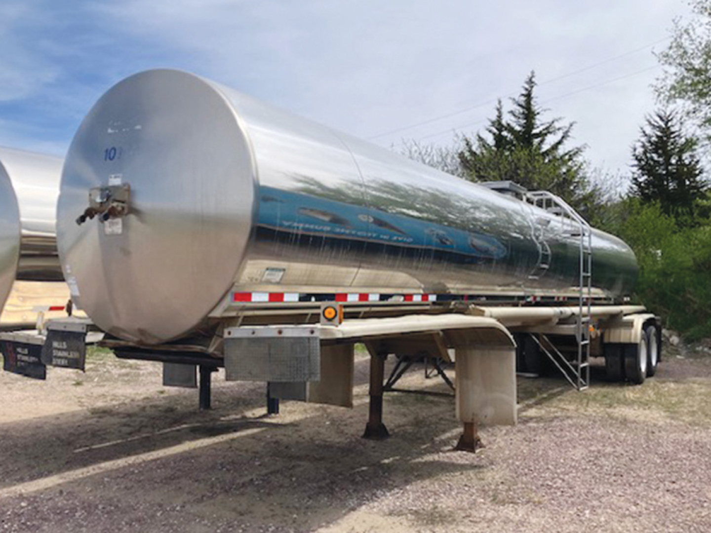 Tank trailer showing reflective stainless steel tanker with ladder and support legs.