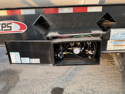 Trailer undercarriage showing a service panel with gauge, valves, and wiring. Labels and stickers near the panel.
