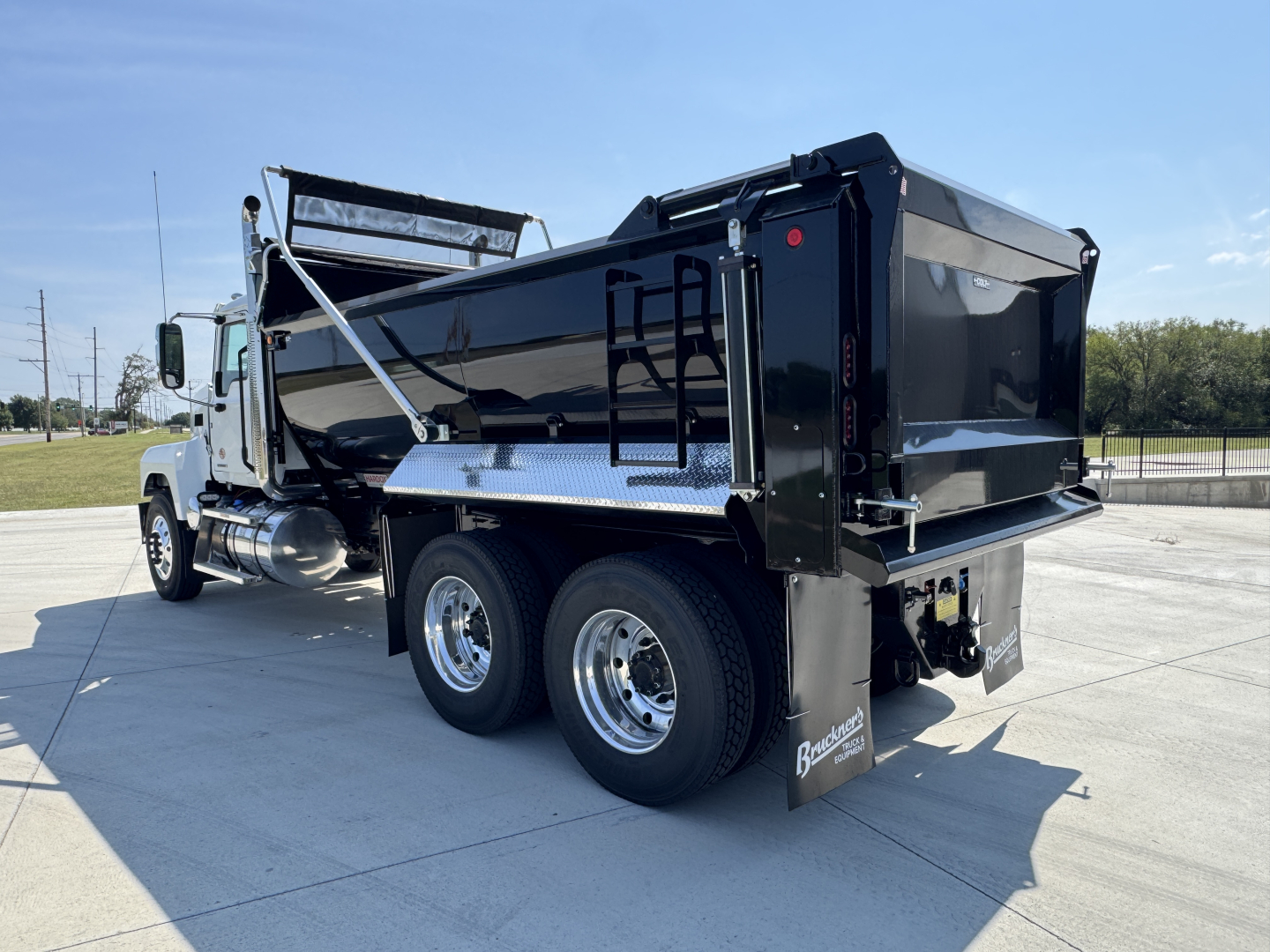 Dump truck rear view showing dual rear axles, black dump bed, and chrome wheels on a 2026 Mack PI64 sample truck.