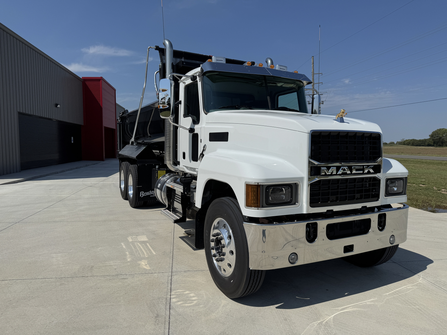 Mack PI64 dump truck in white front-quarter view showing chrome bumper, grille with MACK lettering, dual rear wheels, and dump bed.