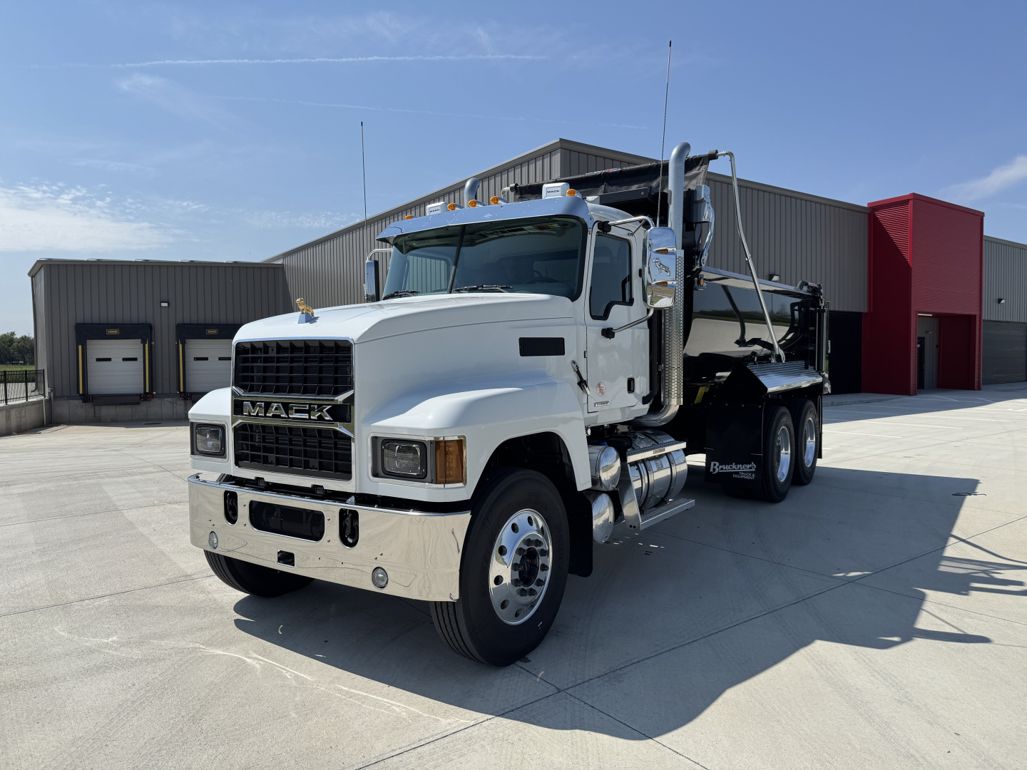 Mack PI64 dump truck in a dealership lot showing front grille with Mack logo and white cab, dual rear wheels, chrome bumper.