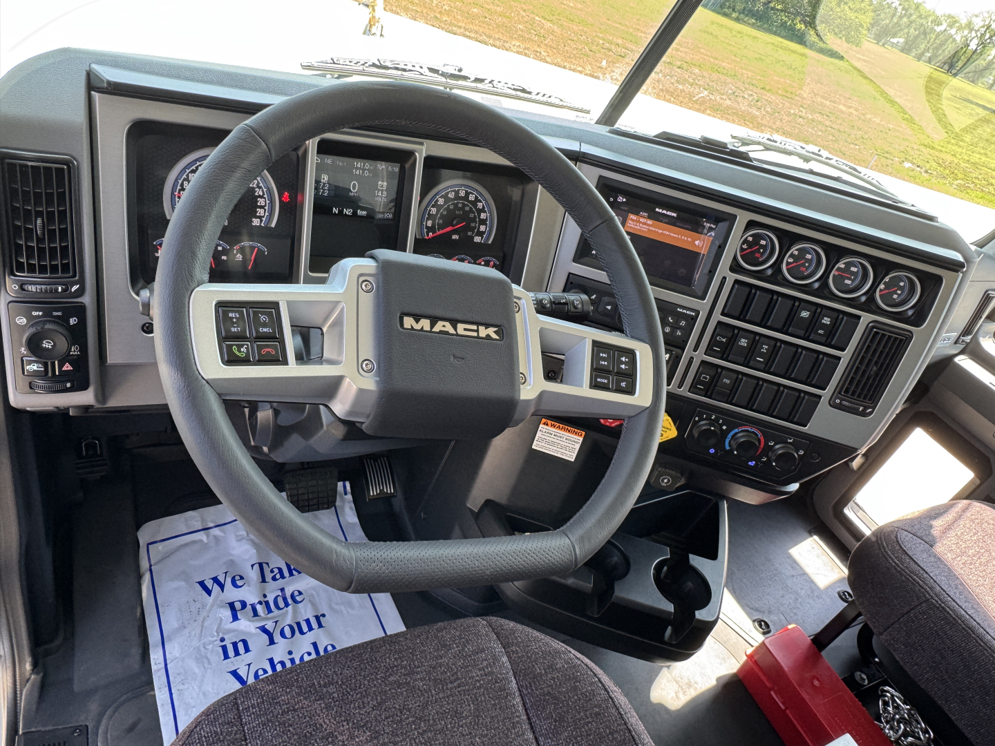 Mack PI64 truck interior showing steering wheel with Mack logo and dashboard gauges, center console with controls, and windshield view.