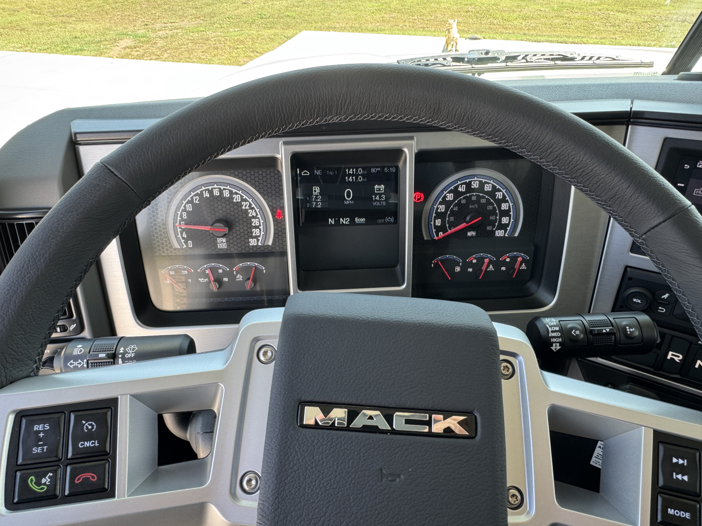 Mack PI64 truck interior showing steering wheel with Mack emblem and instrument cluster with gauges and central display.
