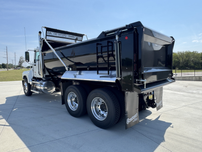 Dump truck rear view showing dual rear axles, black dump bed, and chrome wheels on a 2026 Mack PI64 sample truck.