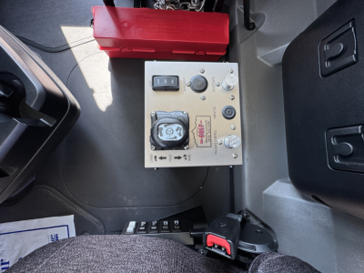 Dashboard area of a new Mack PI64 dump truck showing a control panel with a square digital gauge, a fuse box, and a red battery box.