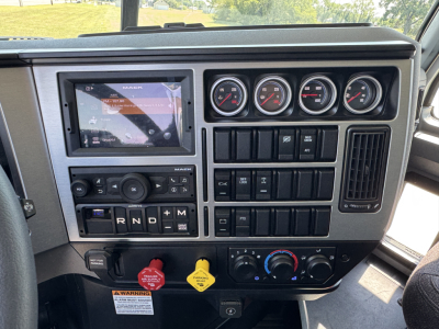 Dashboard of a Mack PI64 truck showing multiple gauges, touchscreen display, gear shifter (R N D), and control switches.
