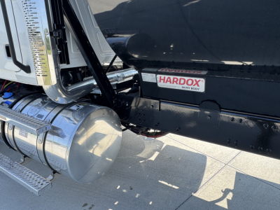 Truck side view showing chrome fuel tank, steps, and Hardox label on the dump bed with glossy black paint.
