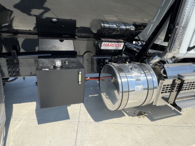 Mack PI64 truck fuel tank and battery box area showing chrome cylindrical air tanks and black toolbox with warning label, side view.