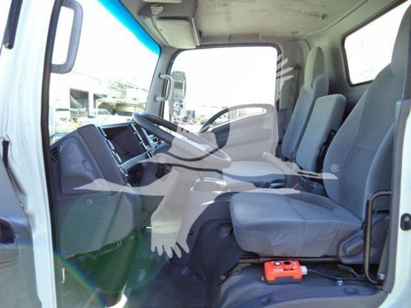 Isuzu NPR HD cab interior showing steering wheel, dashboard, and front seats with orange device on floor mat.