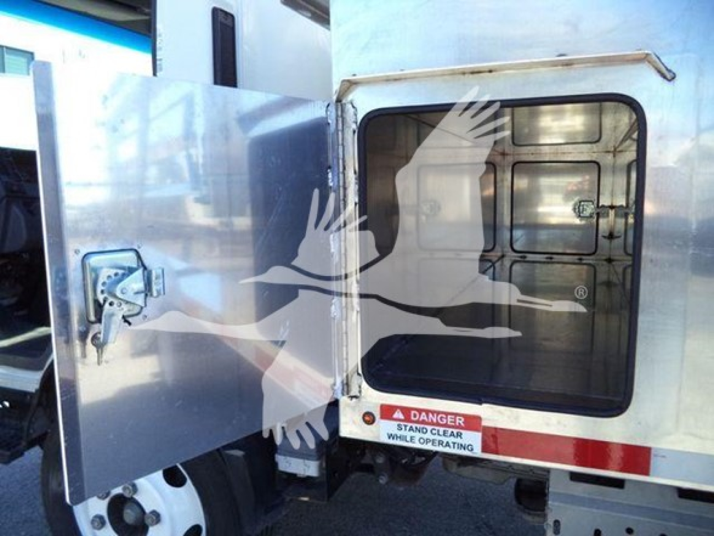 Isuzu NPR HD truck cargo area door open showing rear cabin window and warning label.