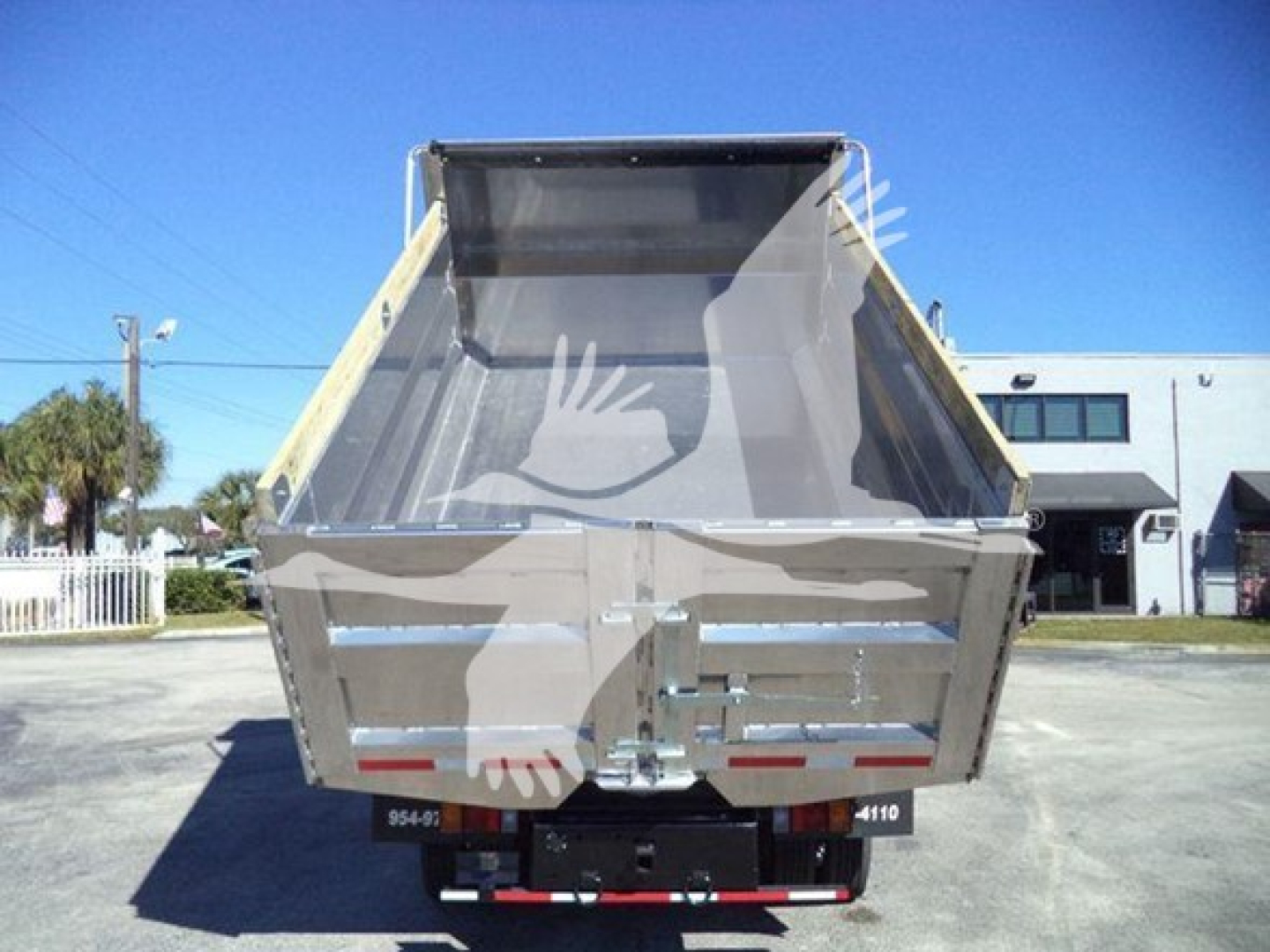 Dump bed of a 2020 Isuzu NPR-HD truck showing metal cargo bed with tailgate and hydraulic mechanism in a used truck lot.