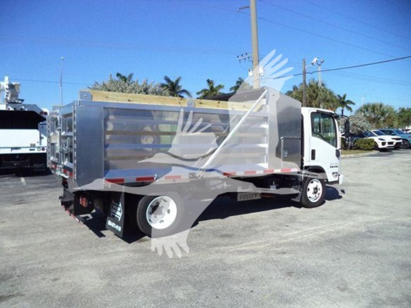 Isuzu NPR HD dump truck in a lot, side view showing a metal cargo bed with horizontal slats, white cab, black mud flaps, and tires.
