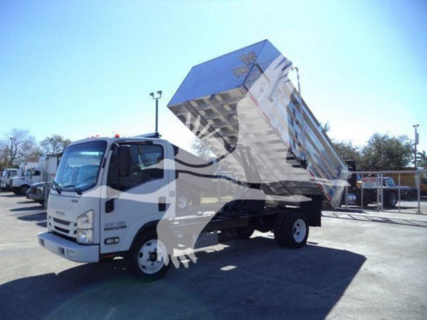 Isuzu NPR HD dump truck with raised dump bed, front cab in view, light blue sky background.
