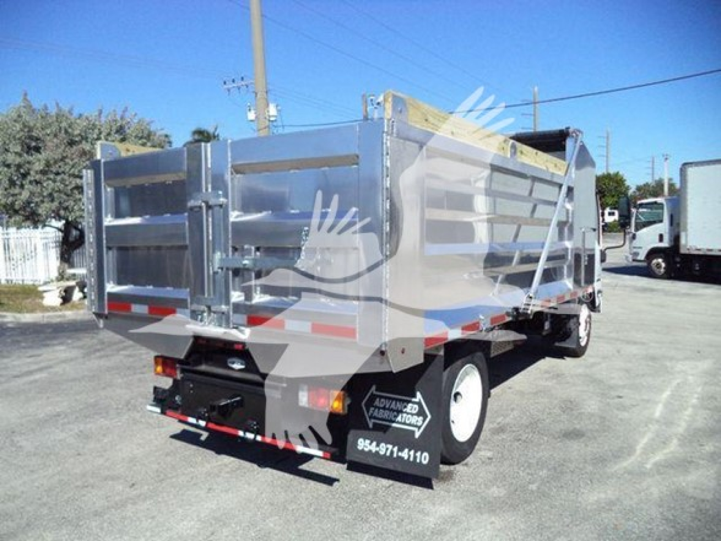 Isuzu NPR-HD dump truck bed in rear three-quarter view showing metallic cargo bed with reflective stripes and rear bumper.