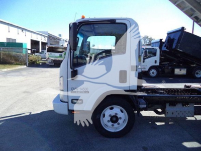 Isuzu NPR HD truck cab side view showing GVW 14500 label and wheel, with dump bed area and surrounding yard.