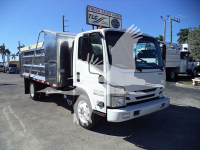 Isuzu NPR-HD dump truck in profile view showing cab and aluminum dump body with GMC logo on grille and front bumper; dealership lot in background.
