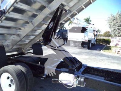 Truck chassis with dump body raised showing hydraulic cylinders and drivetrain components under Isuzu NPR HD cab