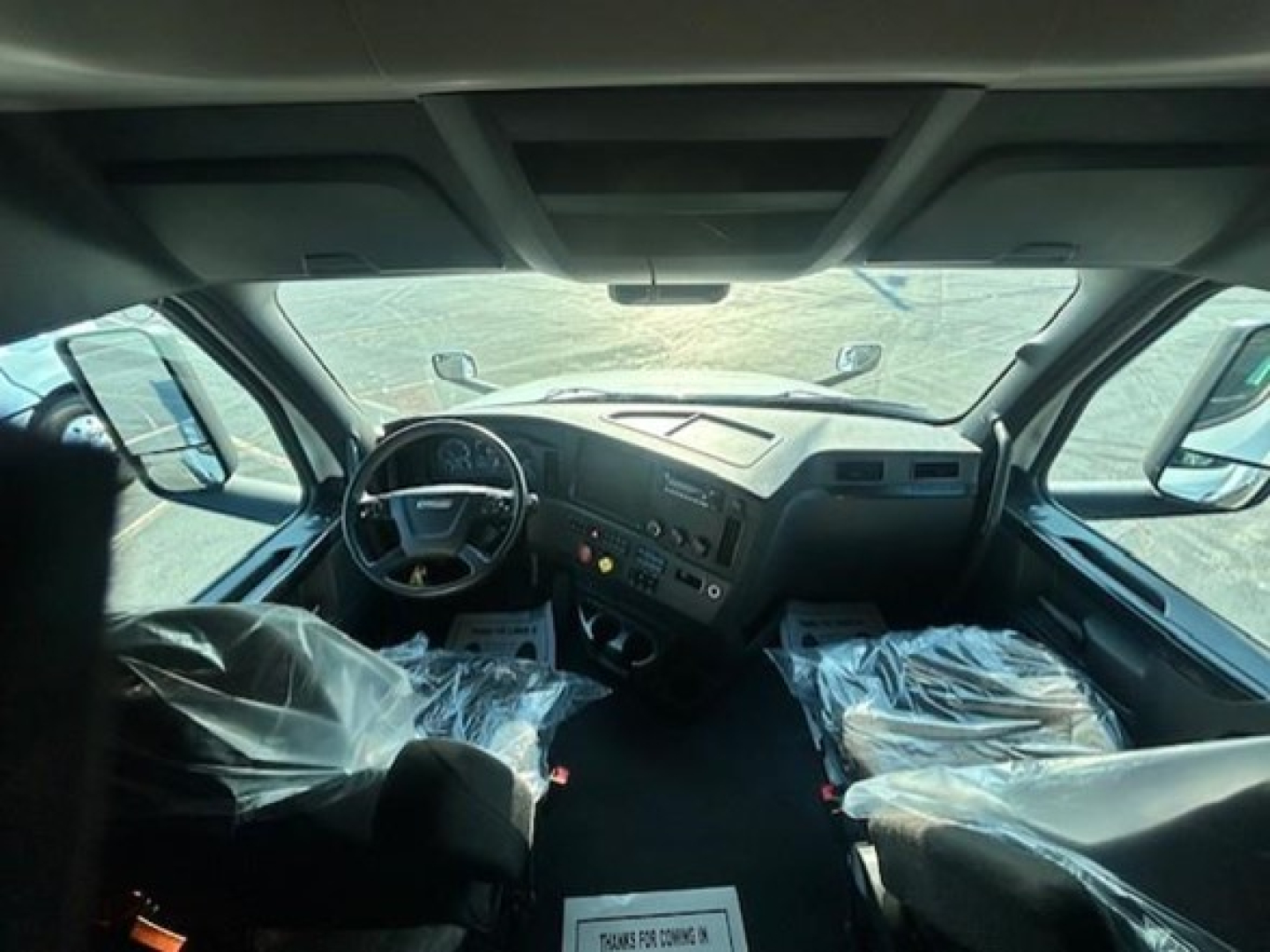 Cab interior of 2023 Freightliner Cascadia 126 truck showing steering wheel and dashboard with plastic-covered seats.