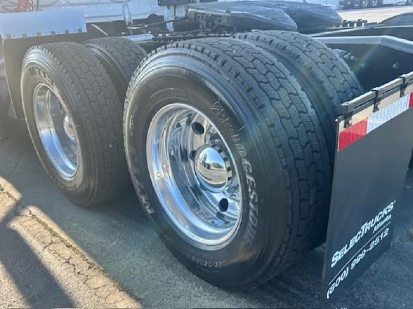Wheel/tire area of a Freightliner Cascadia 126 with dual rear axles and chrome rims; visible tire tread and a mudflap with partial text.