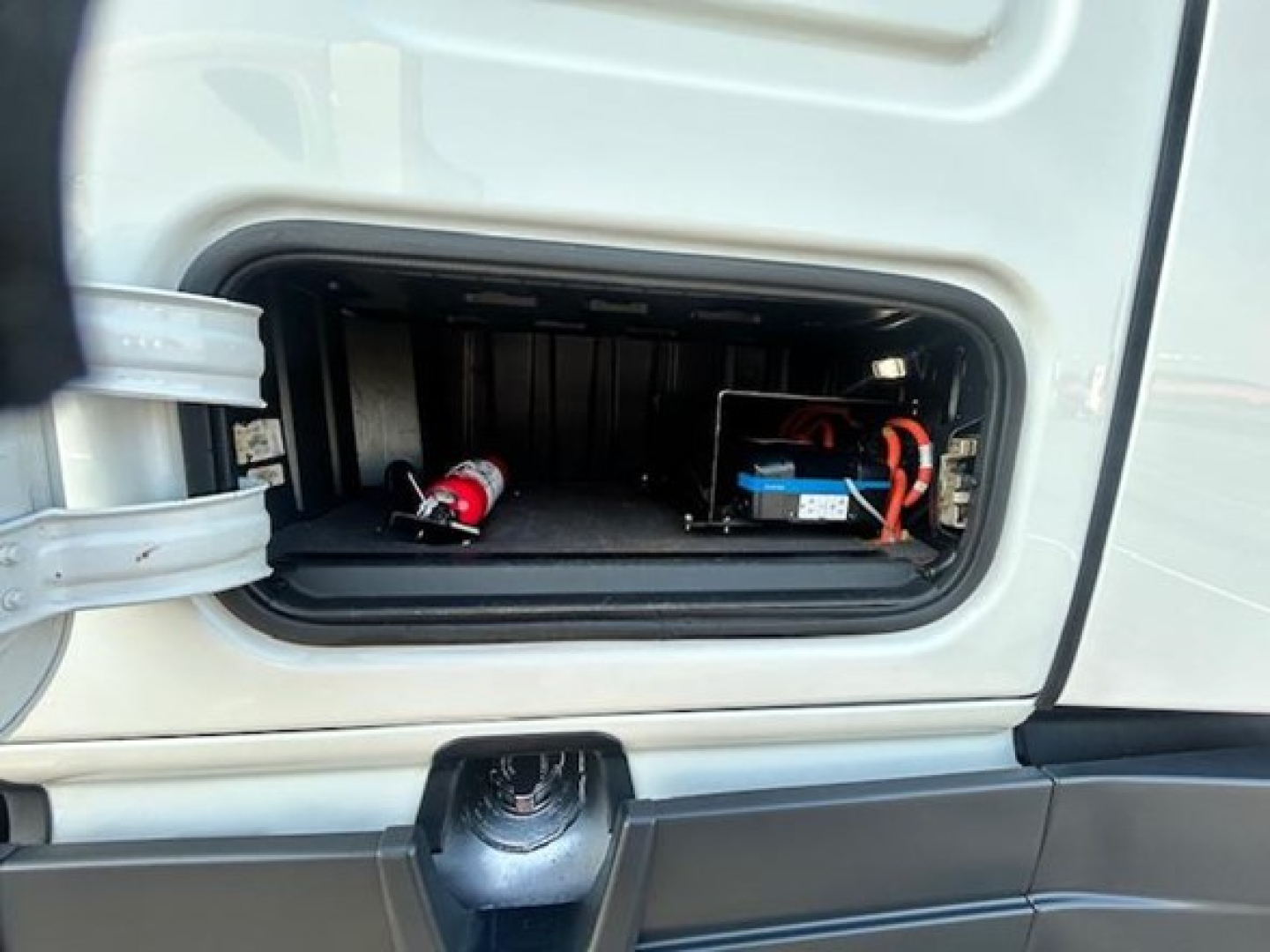 Truck exhaust/compartment door open showing a red fire extinguisher and a battery or electrical box inside the side compartment of a Freightliner Cascadia 126.