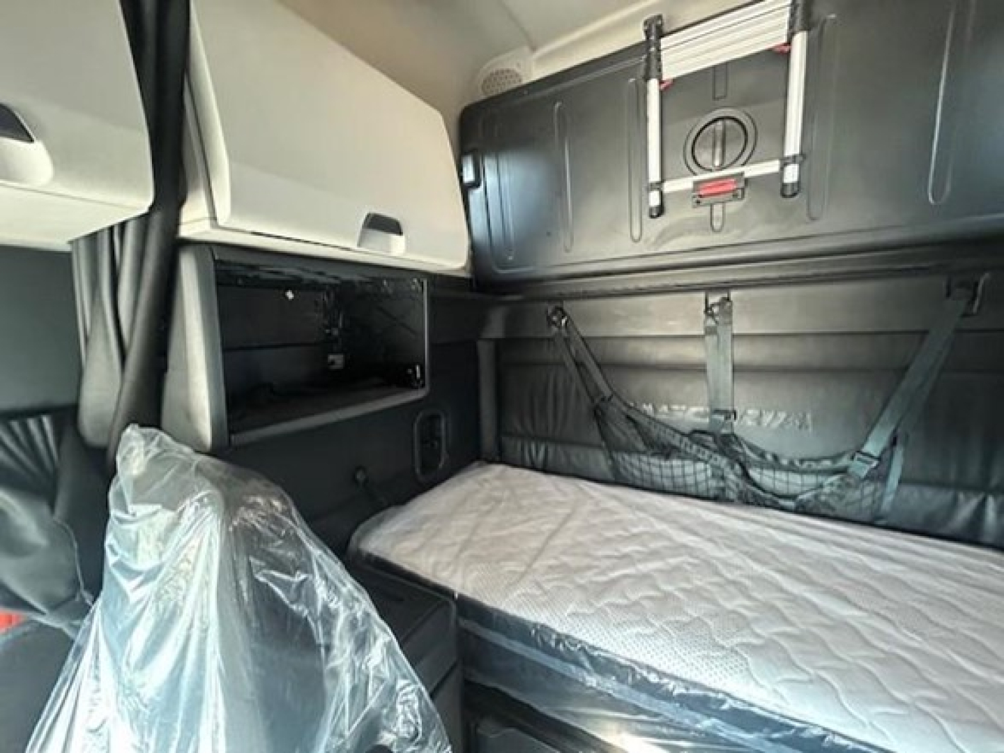 Truck cab interior showing sleeper bunk area with mattress, storage pockets, and overhead cabinets inside a Freightliner Cascadia 126.