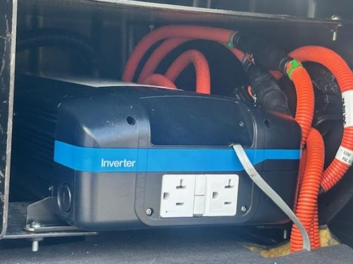 Inverter mounted in Freightliner Cascadia engine bay with red and orange cables and a white dual-wall outlet visible.