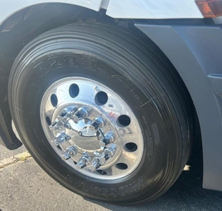 Truck wheel and fender of a Freightliner Cascadia 126 showing chrome hub and tire sidewall.