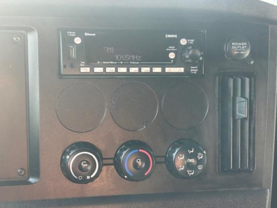 Dashboard panel showing a radio unit with FM1 101.5 MHz and multiple control knobs; circular vents; climate control dials; power outlet; vertical vent on right.