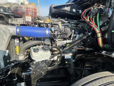 Freightliner Cascadia engine bay showing blue hose, hoses, wiring harness, and reservoir cap in view.