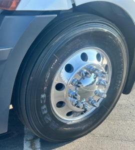 Truck wheel close-up showing polished chrome dual rear axles and Bridgestone tire with visible lug nuts on a Freightliner Cascadia sleeper cab.