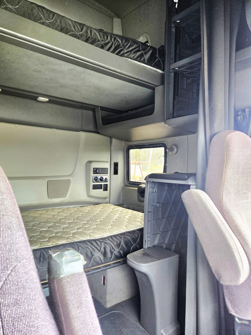 Interior of a used 2020 International condo sleeper showing a lower bunk and upper bunk, side storage, and captain chair in the cab.