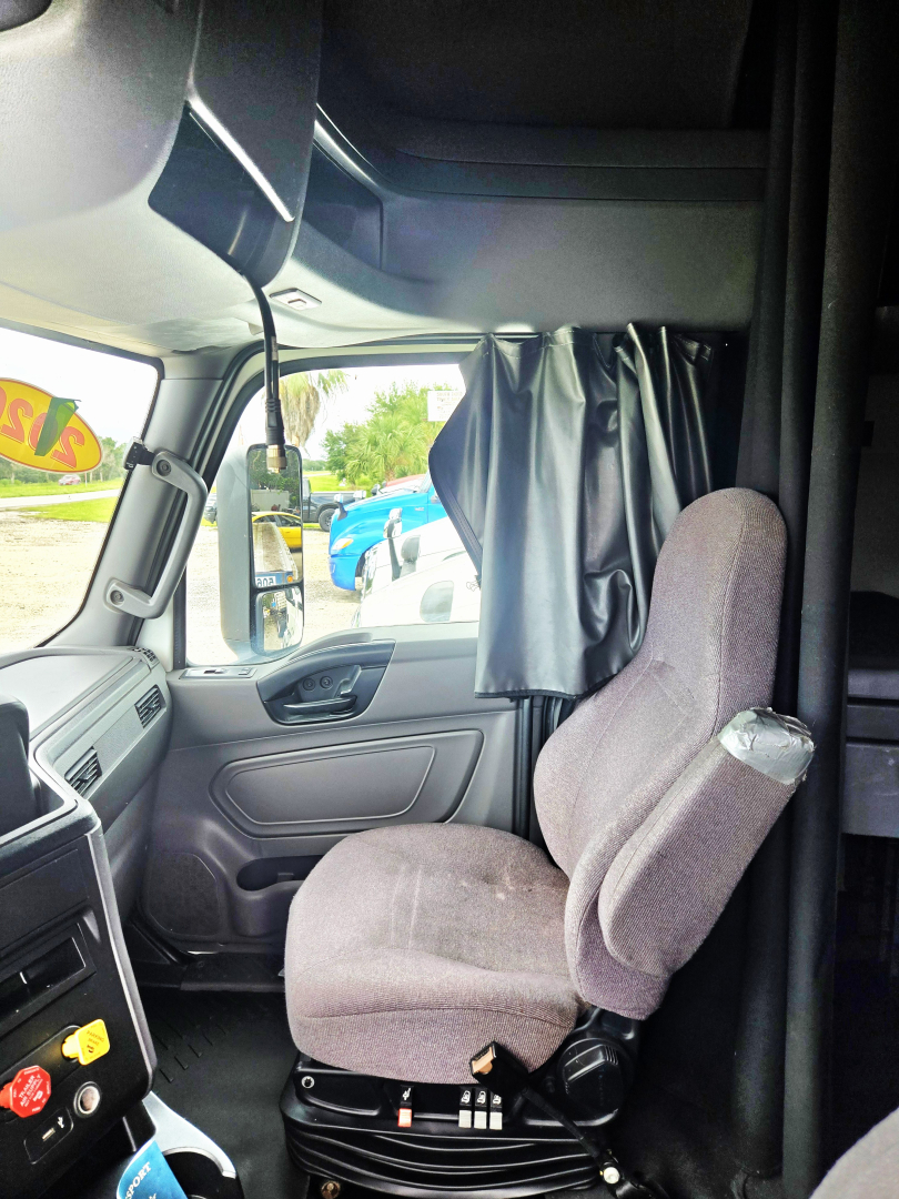 Truck cab interior showing driver seat, steering wheel, and partition curtain in a 2020 International CONDO double bunk sleeper.