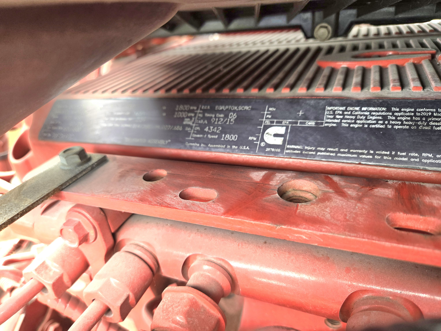 Label plate inside a truck engine bay with technical specifications and warnings, partially obscured by metal frame.