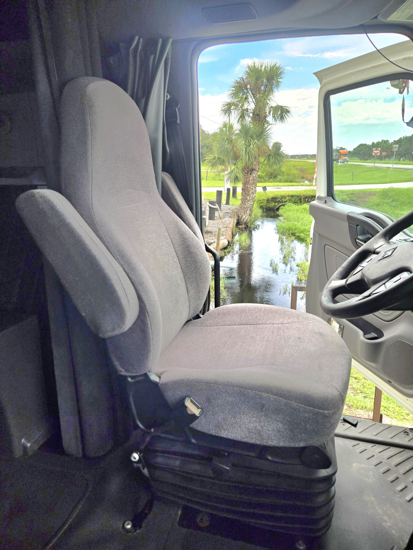 Truck cab seat inside International CONDO double bunk sleeper showing driver seat and steering wheel.