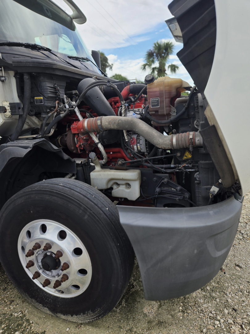 Truck engine bay visible with front left wheel, showing hoses, coolant reservoir, and engine components in a CONDO double bunk sleeper truck.