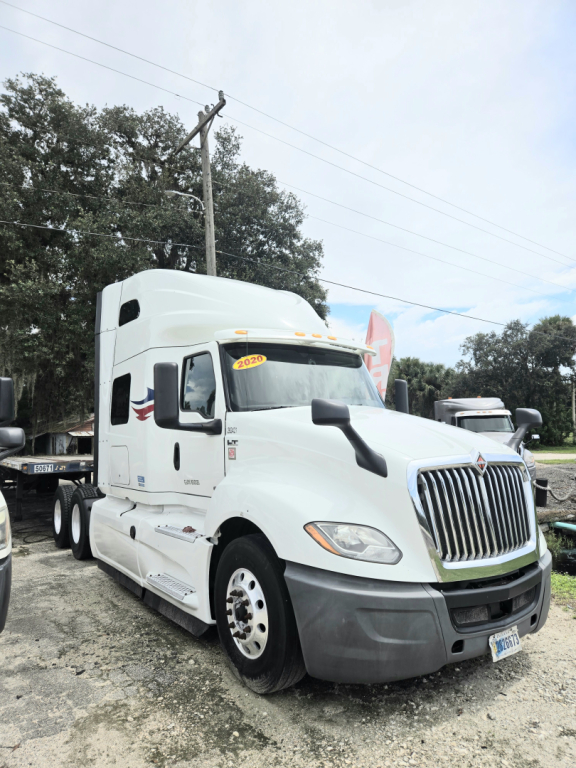Truck cab showing International CONDO sleeper with double bunk, white exterior, grille, and front bumper; dealership lot in background.